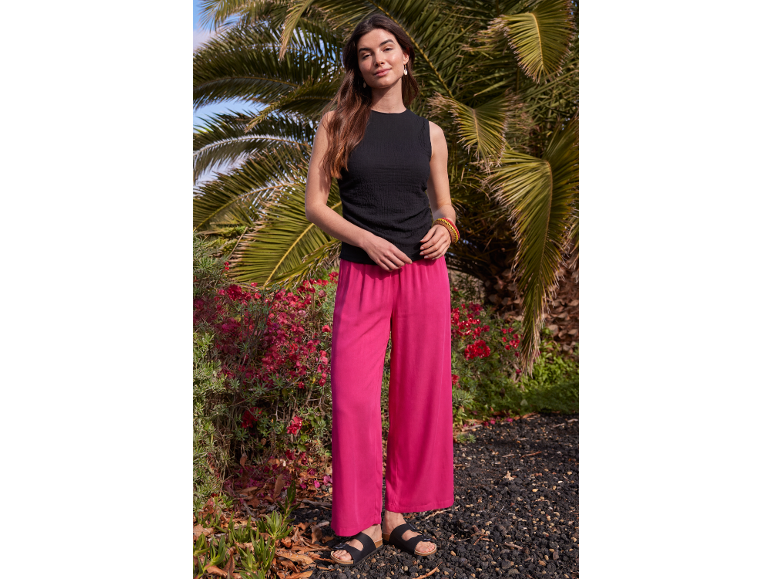 Donna con top nero e pantaloni ampi rosa acceso davanti a palme.