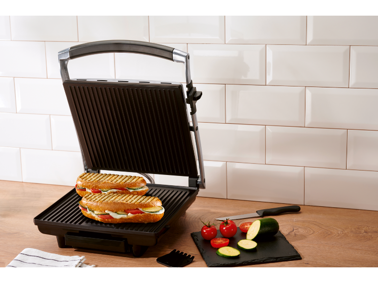 Piastra per panini con due panini grigliati e verdure fresche in cucina.