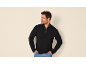 Uomo in maglione nero con cerniera e jeans, mani nelle tasche.