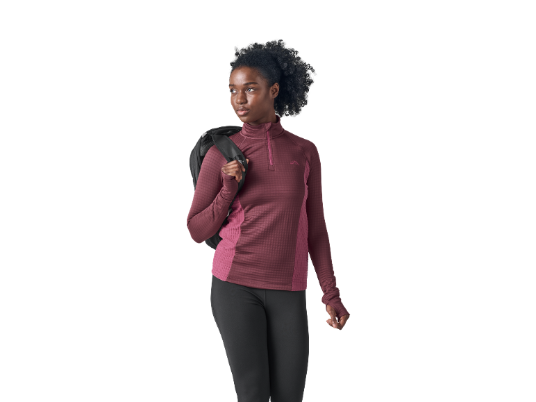 Donna con top a maniche lunghe bordeaux con mezza zip e leggings neri, con uno zaino.