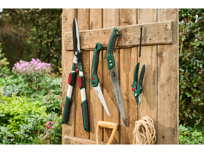 Forbici da giardino, seghe e cesoie appese a una parete di legno davanti a un giardino.