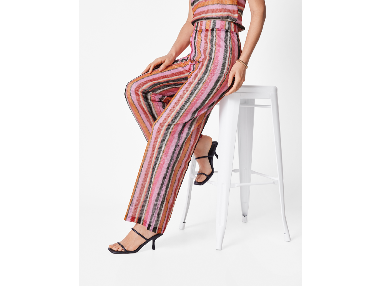 Donna con pantaloni e top a righe colorate, seduta su uno sgabello bianco.