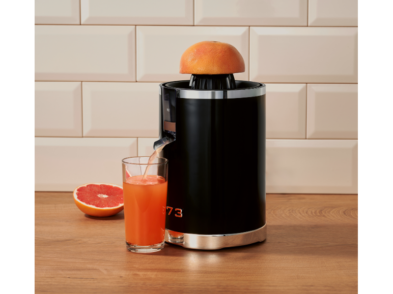 Spremiagrumi nero con mezzo pompelmo sopra, che versa il succo in un bicchiere su un tavolo di legno.