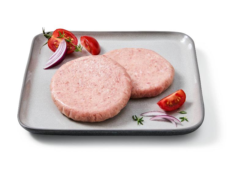 Due hamburger crudi su un piatto con pomodori, cipolla rossa ed erbe aromatiche.