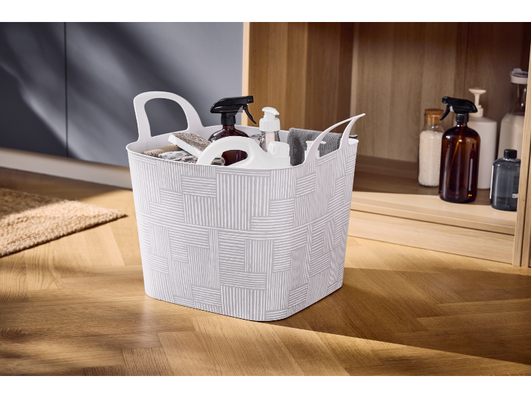 Cesto bianco con prodotti e accessori per la pulizia su pavimento in legno.