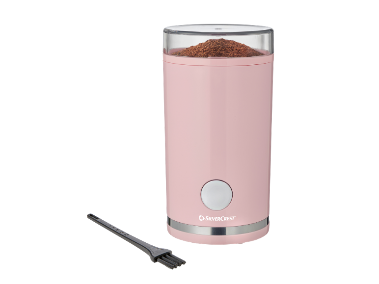 Macinacaffè rosa con caffè macinato e spazzola per la pulizia.