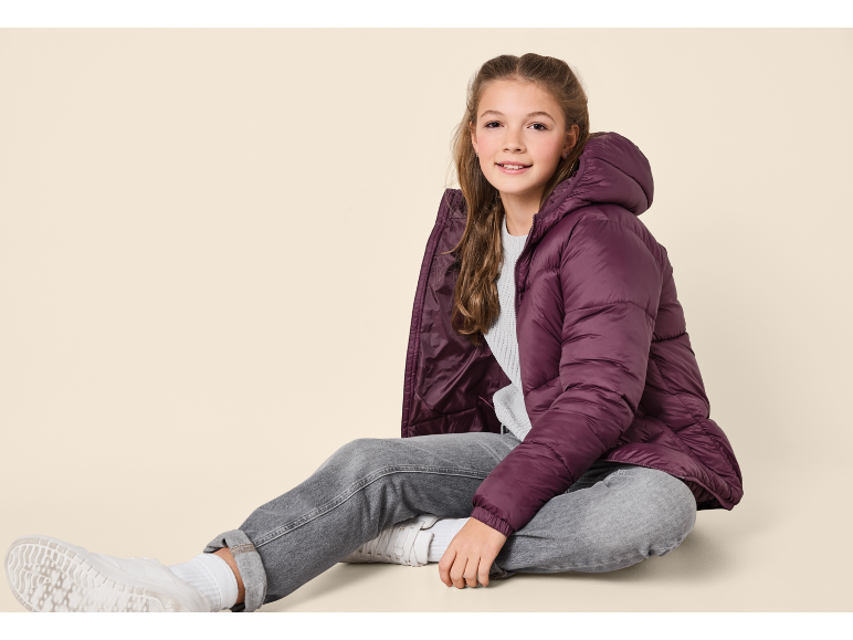 Ragazza con piumino viola, jeans grigi e scarpe da ginnastica bianche.