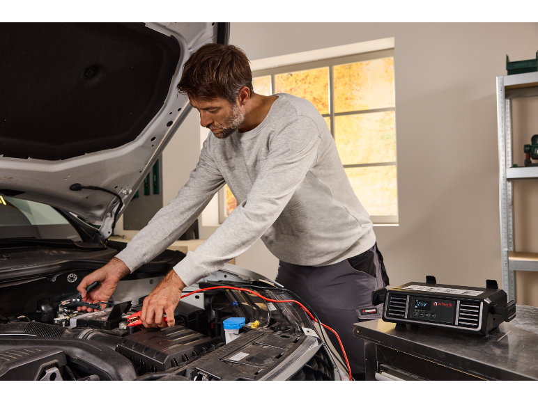 Uomo che collega un caricabatterie per auto a una batteria sotto il cofano aperto.