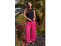 Donna con top nero e pantaloni ampi rosa acceso davanti a palme.