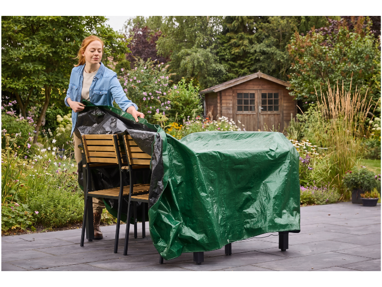 Donna che copre i mobili da giardino con un telo verde su un patio.