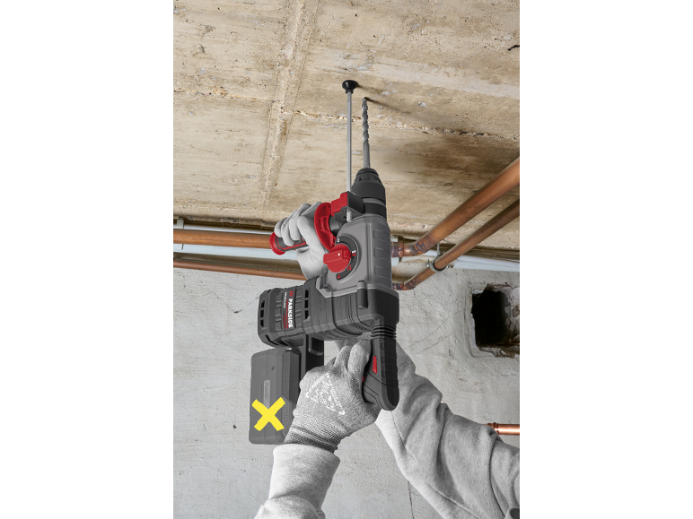 Trapano a percussione a batteria che fora un soffitto di cemento.
