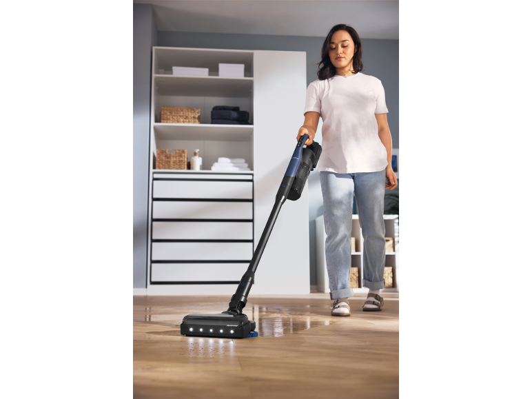 Donna pulisce un pavimento in legno con un aspirapolvere senza fili con funzione lavapavimenti.