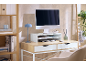 Scrivania da ufficio con computer, supporto monitor, lampada blu e scaffalature in legno.