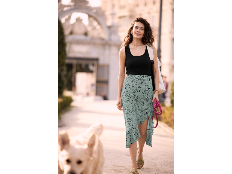 Donna in top nero e gonna a pois che cammina con un cane.