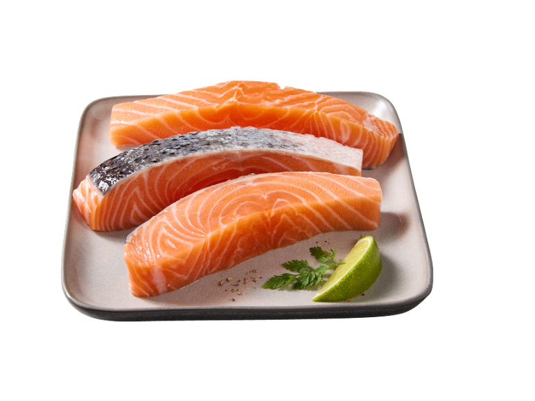Tre pezzi di salmone fresco con pelle, uno spicchio di lime e prezzemolo su un piatto.