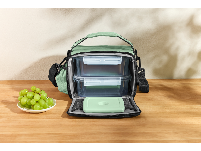 Borsa termica verde con contenitori per alimenti e impacco di ghiaccio, con uva accanto.