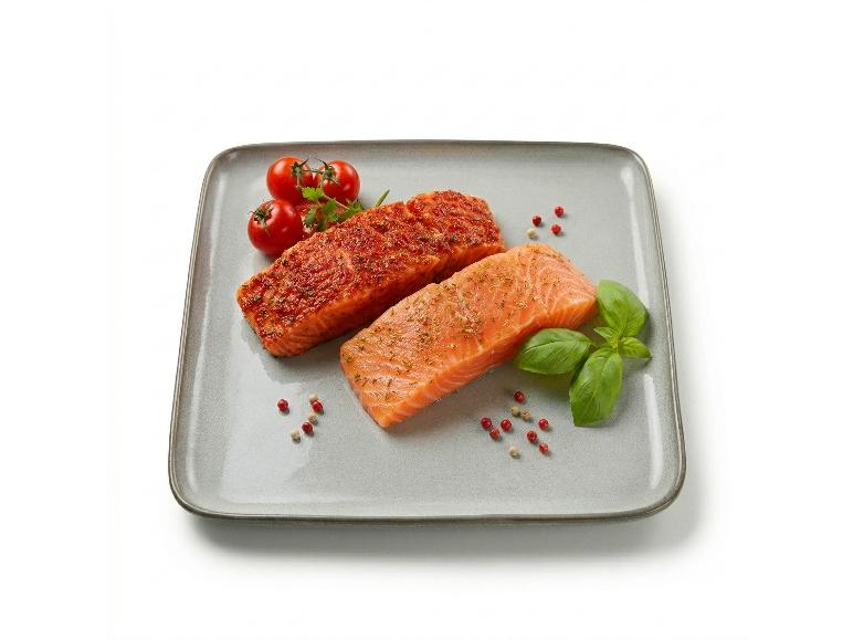 Due filetti di salmone conditi con pomodorini e basilico su un piatto grigio.