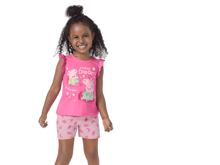 Bambina sorridente in pigiama rosa con 'Sweet Dreams' e personaggi maialino, e pantaloncini a fantasia.