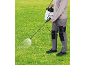 Persona che spruzza erba con uno spruzzatore da giardino con tracolla.