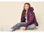 Ragazza con piumino viola, jeans grigi e scarpe da ginnastica bianche.