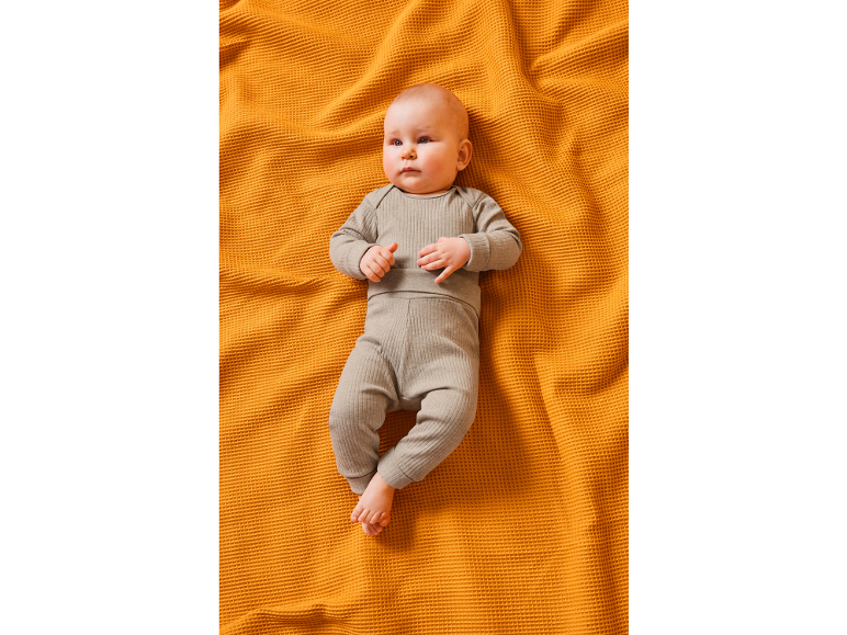 Bebè in completo a costine grigio su una coperta arancione.