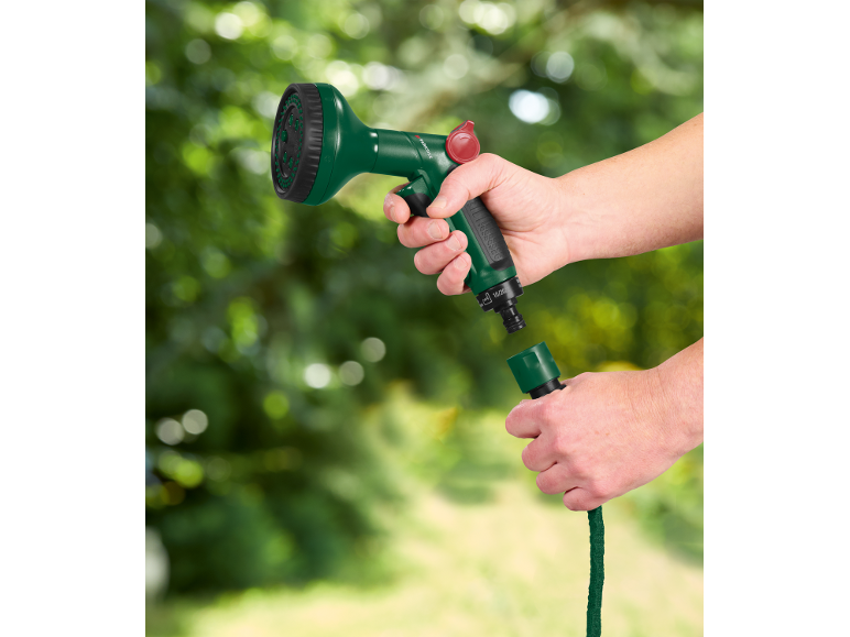 Mani che collegano un ugello verde per tubo da giardino a un tubo da giardino verde.