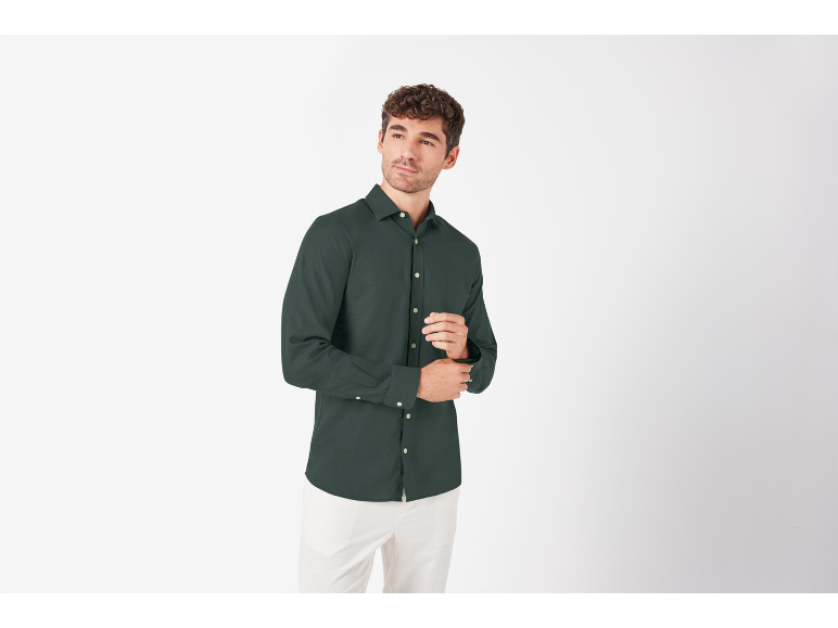 Uomo in camicia verde scuro a maniche lunghe e pantaloni bianchi, che si sistema il polsino.