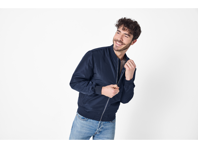 Uomo sorridente con giubbotto bomber blu scuro e jeans.