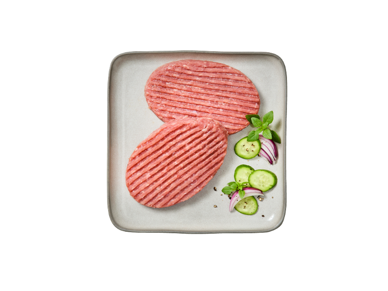 Due hamburger di carne cruda su un piatto con cetrioli, cipolla rossa e basilico.
