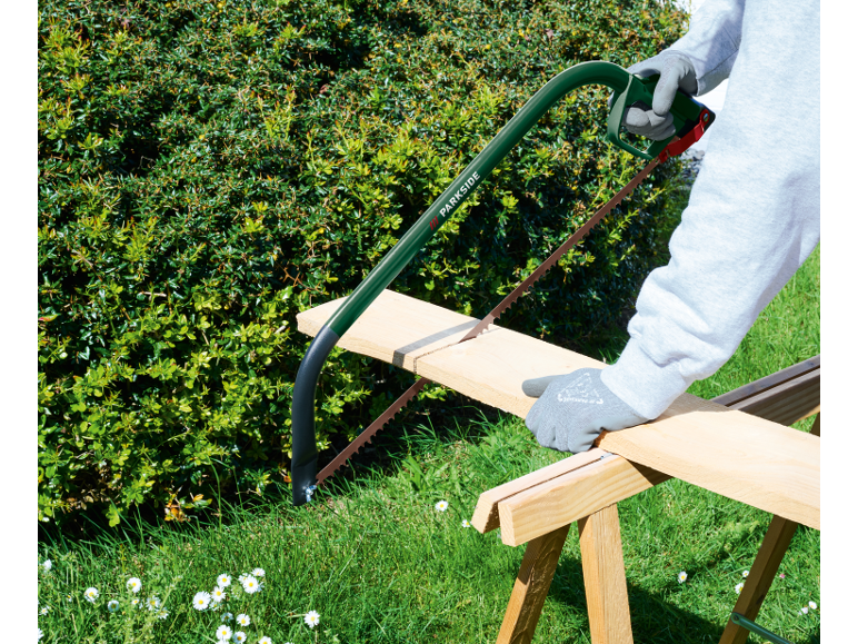 Persona che taglia una tavola di legno con una sega ad arco in un giardino.