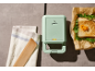 Piastra per sandwich verde con spia luminosa, asciugamano e sandwich tostato con rucola.