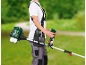 Persona con un decespugliatore a benzina su sfondo di paesaggio verde sfocato.