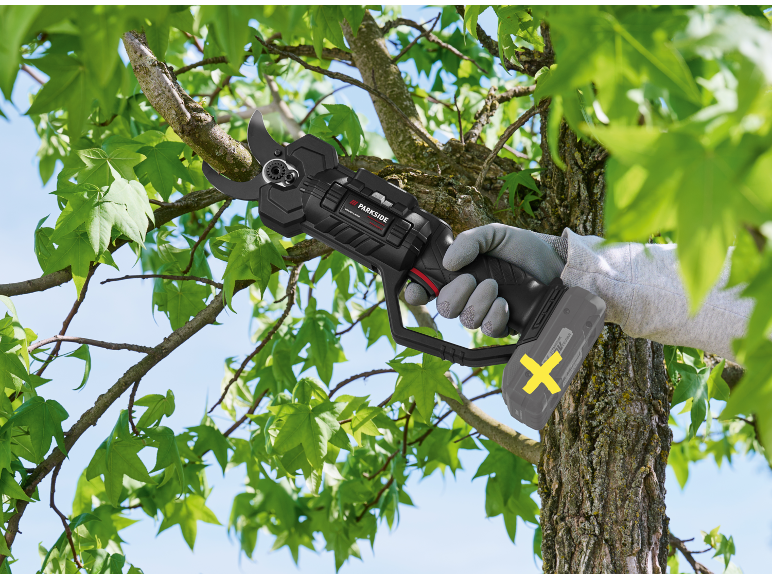 Forbici da potatura a batteria che tagliano un ramo d'albero, foglie verdi visibili.