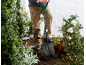Persona che scava nel terreno con una pala in un giardino con piante e rose.