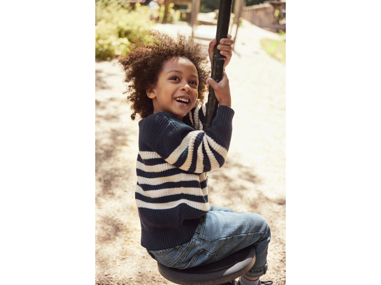 Bambino felice con maglione a righe e jeans, che gioca all'aperto.