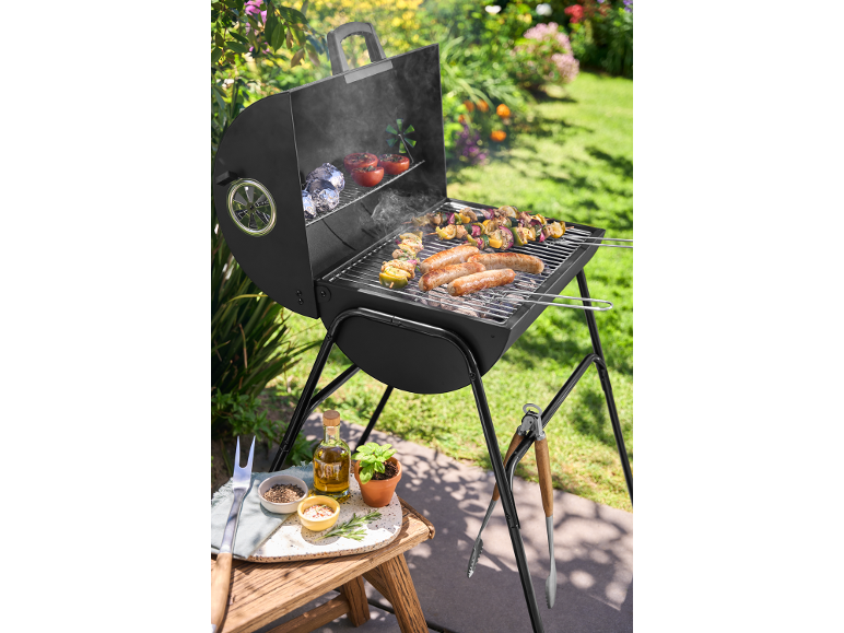 Barbecue a carbone con salsicce, spiedini e verdure grigliate in un giardino soleggiato.