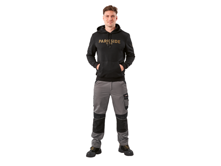 Uomo con felpa con cappuccio nera e pantaloni da lavoro grigi.