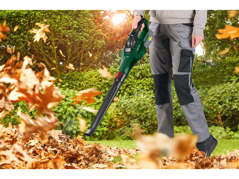 Uomo con soffiatore elettrico per foglie che pulisce foglie secche in giardino.