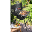 Barbecue a carbone con salsicce, spiedini e verdure grigliate in un giardino soleggiato.