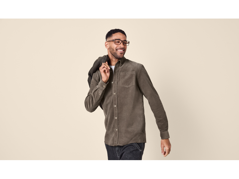 Uomo con camicia di velluto a coste marrone e occhiali, con una giacca sulla spalla.