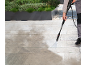 Persona che pulisce un patio con un'idropulitrice, mostrando i risultati prima e dopo.