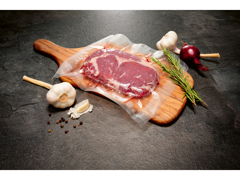 Bistecca sottovuoto su tagliere con aglio, rosmarino e cipolla.