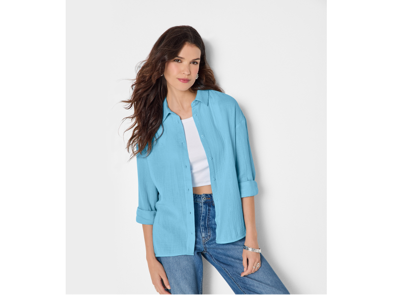 Donna con camicia azzurra, top bianco e jeans, con orecchini e bracciali.