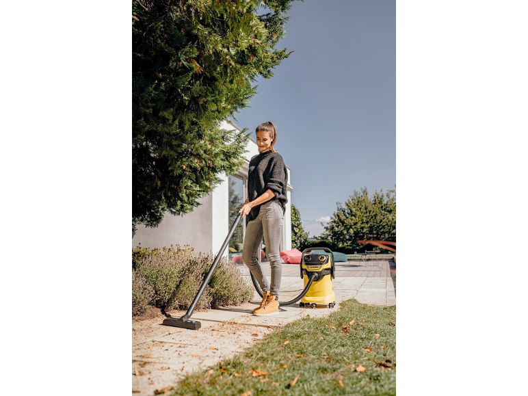 Donna che aspira un patio con un aspirapolvere da officina giallo.