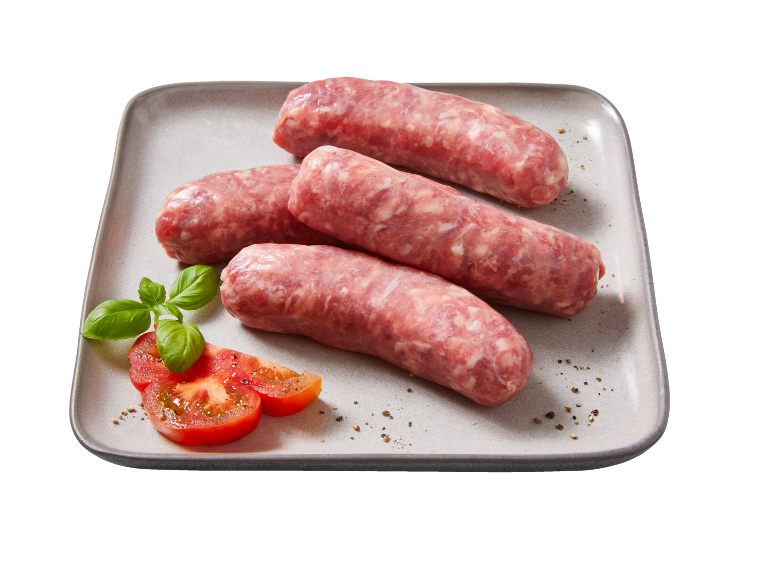 Salsicce crude con fette di pomodoro e basilico su un piatto.