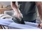 Una persona stira una camicia azzurra su un asse da stiro con un ferro scuro.