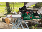 Motosega a batteria verde che taglia un tronco di legno su un cavalletto in un ambiente esterno.