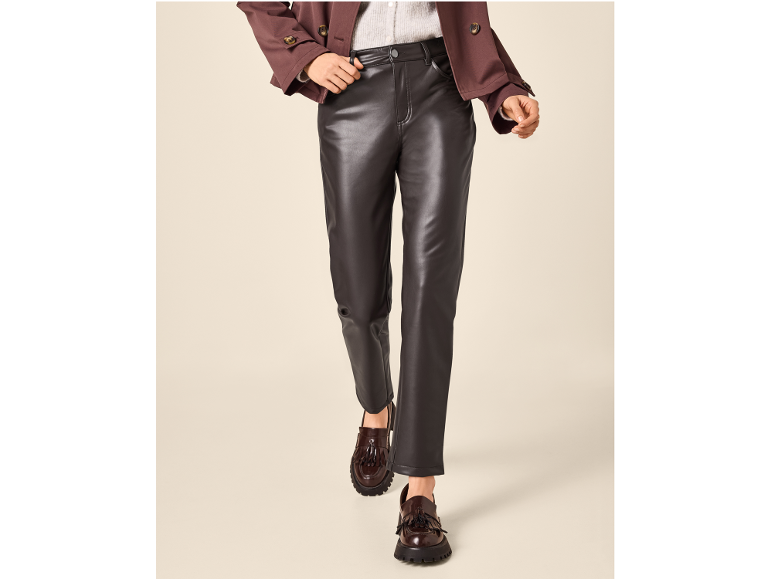 Donna con pantaloni in pelle scura, giacca marrone e mocassini con nappe