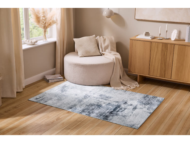 Angolo soggiorno con pouf rotondo, tappeto chiaro e credenza in legno.