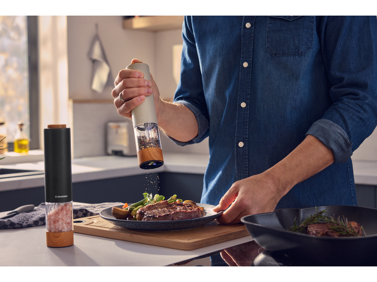 Uomo che condisce una bistecca con un macinapepe elettrico in cucina.